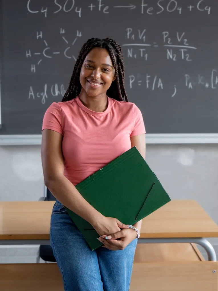 A smiling student holding a green folder in a classroom